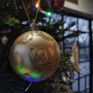 A close-up view of a bauble on a Christmas Tree. The interior of the Little Theatre foyer windows are visible in the background