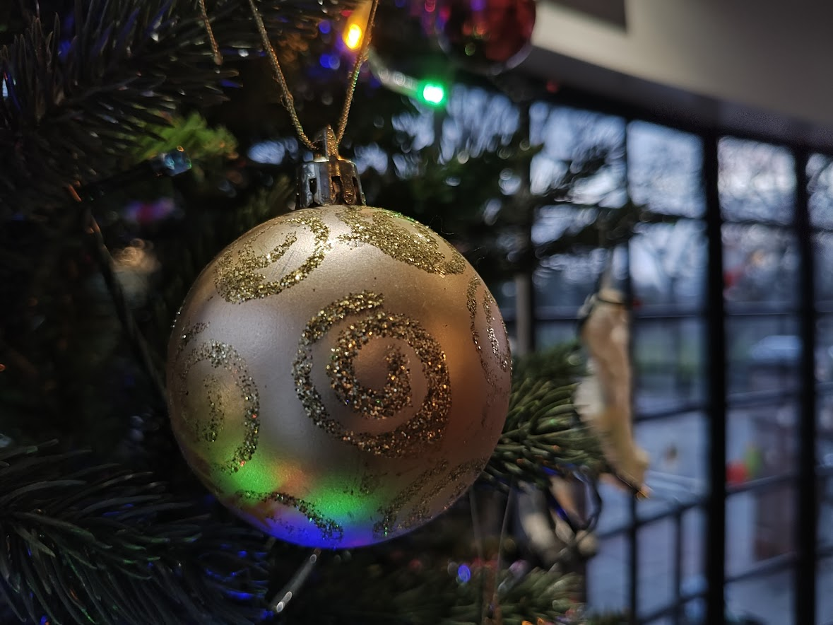 A close-up view of a bauble on a Christmas Tree. The interior of the Little Theatre foyer windows are visible in the background
